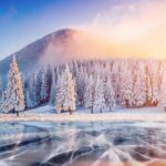 Cracks on the surface of the blue ice. Frozen lake in winter mountains. It is snowing. The hills of pines. Carpathian Ukraine Europe.