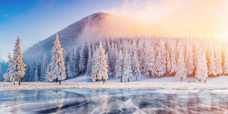 Cracks on the surface of the blue ice. Frozen lake in winter mountains. It is snowing. The hills of pines. Carpathian Ukraine Europe.