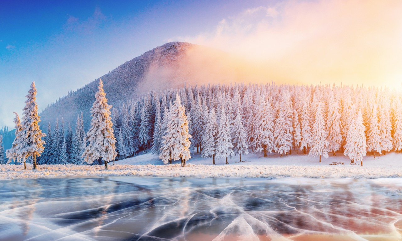 Cracks on the surface of the blue ice. Frozen lake in winter mountains. It is snowing. The hills of pines. Carpathian Ukraine Europe.